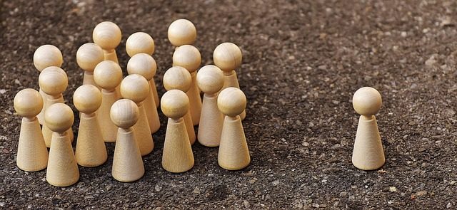 Viele Holzfiguren als Gruppe, eine einzelne Figur steht daneben